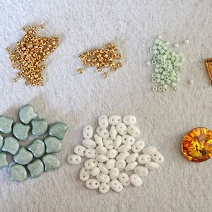 May include: Assortment of beads in various colors and shapes, including gold, white, and light green. There is also a single, large, orange crystal bead.