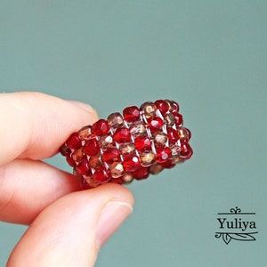 May include: A red and gold beaded ring. The ring is made of small, square beads that are woven together in a pattern.