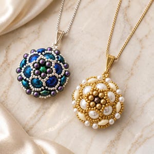 May include: Two round beaded pendants on chains. The left pendant features iridescent blue, green, and purple beads in a floral pattern. The right pendant features cream, white, and gold-toned beads in a similar circular, textured arrangement.