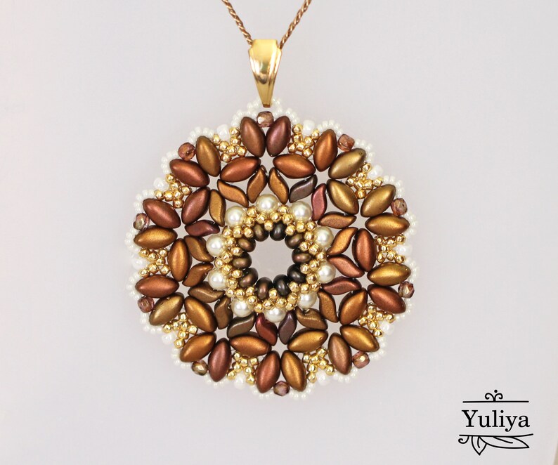 May include: A gold pendant necklace with a round, beaded design. The beads are in shades of brown, gold, and white, creating a floral pattern.