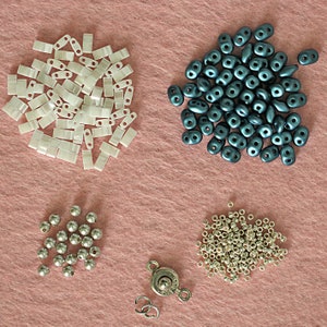 Op de afbeelding: Assortiment van kralen in verschillende vormen, maten en kleuren, waaronder wit, zilver en donkerblauw. Er is ook een zilveren sluiting.