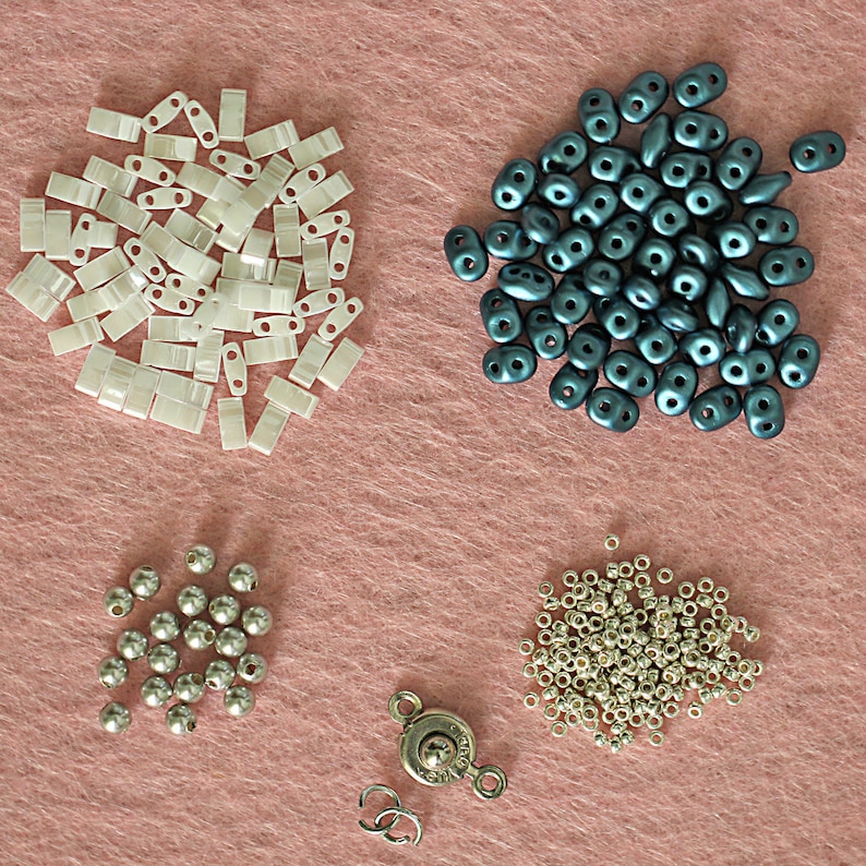 Op de afbeelding: Assortiment van kralen in verschillende vormen, maten en kleuren, waaronder wit, zilver en donkerblauw. Er is ook een zilveren sluiting.