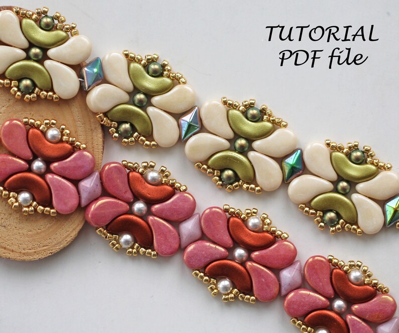 Op de afbeelding: Twee kralenarmbanden met een bloemenmotief. De bovenste armband is wit met groene accenten en de onderste armband is roze met oranje accenten. Beide armbanden hebben gouden kralen.