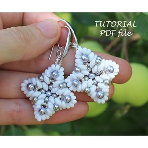 Op de afbeelding: Een paar zilveren stervormige oorbellen met witte en zilveren kralen. De oorbellen worden in een hand tegen een groene achtergrond gehouden. De tekst "TUTORIAL PDF file" is zichtbaar in de rechterbovenhoek van de afbeelding.