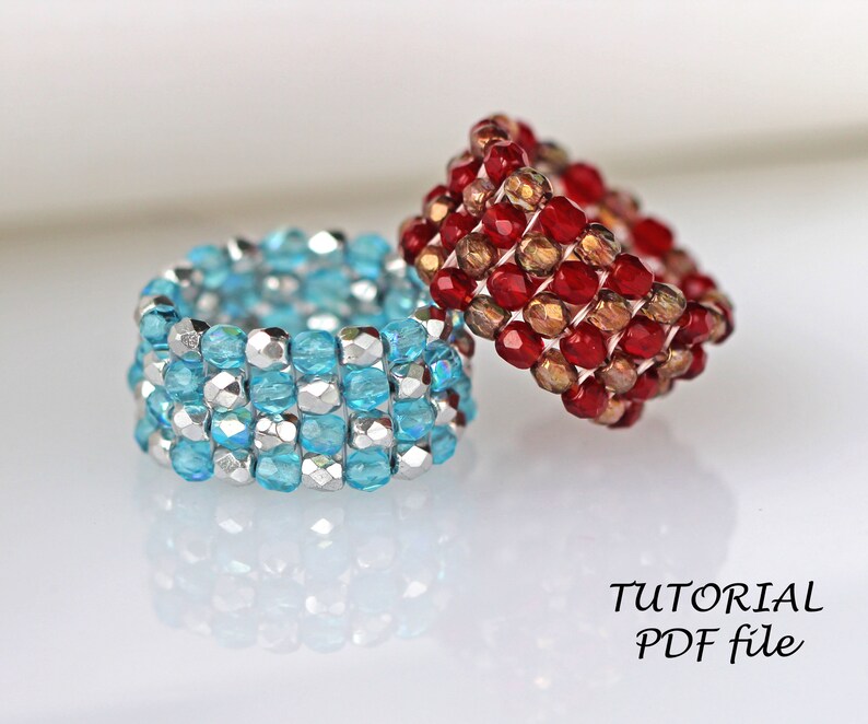 May include: Two beaded rings, one blue and silver, the other red and gold. The rings are stacked on top of each other. The text "TUTORIAL PDF file" is visible below the rings.