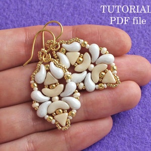 Op de afbeelding: Een paar gouden oorbellen met witte en cr&egrave;mekleurige kralen in een geometrisch patroon. De oorbellen worden in een hand tegen een paarse achtergrond gehouden. De tekst "TUTORIAL PDF file" is zichtbaar in de rechterbovenhoek van de afbeelding.