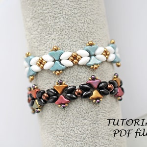 May include: Two beaded bracelets displayed on a grey stand. The top bracelet is white and blue with gold accents. The bottom bracelet is black, red, and gold with purple accents. The text "TUTORIAL PDF file" is visible below the bracelets.
