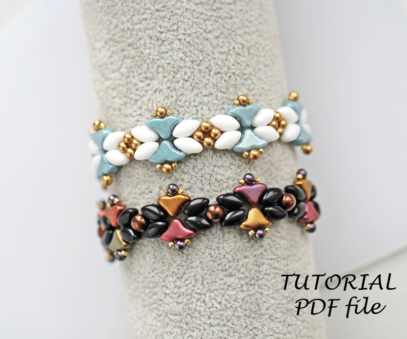 May include: Two beaded bracelets displayed on a grey stand. The top bracelet is white and blue with gold accents. The bottom bracelet is black, red, and gold with purple accents. The text "TUTORIAL PDF file" is visible below the bracelets.