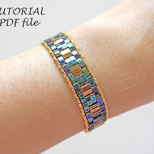 May include: A multi-colored beaded bracelet with gold accents. The bracelet is made with square-shaped beads in shades of blue, green, and copper. The bracelet is worn on a person's wrist.