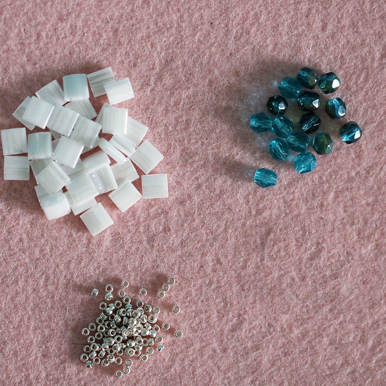May include: Three piles of beads on a pink surface. One pile is white, one is silver, and one is teal.