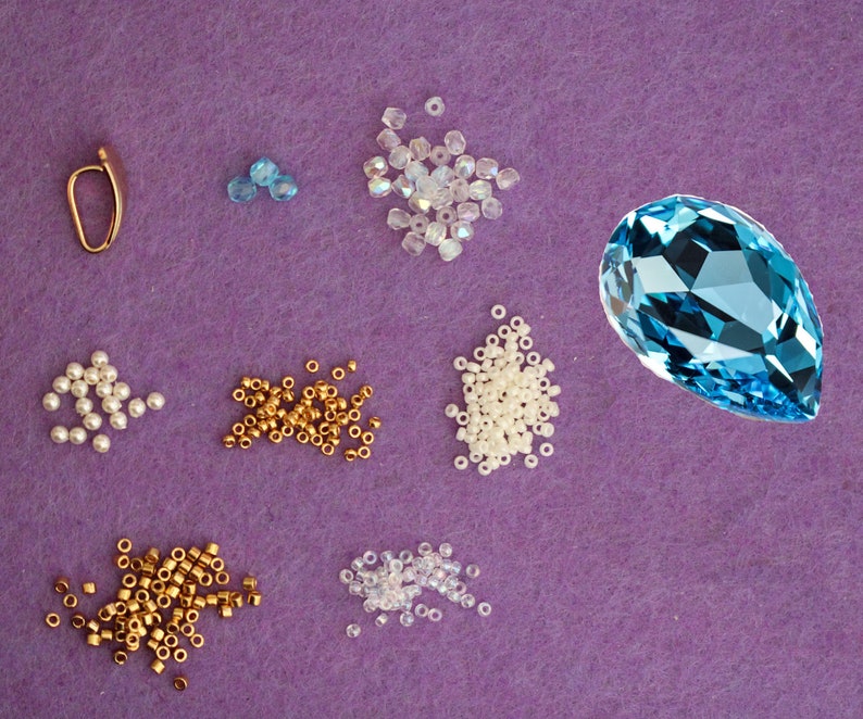 Peut inclure: Assortiment de perles de diff&eacute;rentes couleurs et tailles, notamment blanches, dor&eacute;es et bleues. On trouve &eacute;galement une grosse pierre pr&eacute;cieuse bleue en forme de larme.