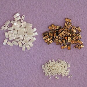 Peut inclure: Trois tas de perles blanches et dor&eacute;es. Le premier tas est blanc et iridescent, le deuxi&egrave;me tas est dor&eacute; et le troisi&egrave;me tas est blanc et rond.