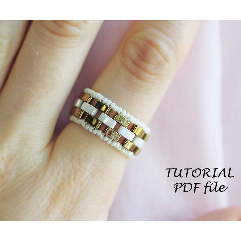 Peut inclure: Une bague en perles blanches, dor&eacute;es et brunes avec un motif g&eacute;om&eacute;trique. La bague est sur un doigt et le texte "TUTORIAL PDF file" est en dessous de la bague.