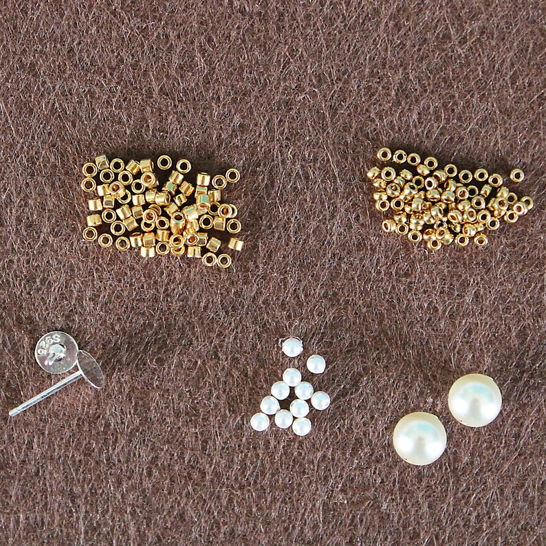 May include: A close-up of jewelry making supplies, including gold beads, white pearls, and a silver earring post.
