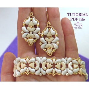 Op de afbeelding: Een set witte en gouden kralen oorbellen en een armband. De oorbellen zijn druppelvormig en de armband is een brede band. De sieraden zijn gemaakt met kralen en hebben een geometrisch patroon.