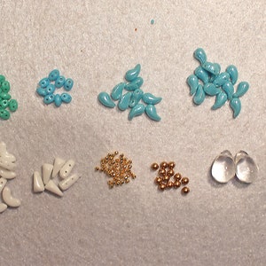 May include: Assortment of turquoise, white, and gold beads, along with two clear glass beads and gold earring hooks. The beads are various shapes, including teardrop, crescent, and round.