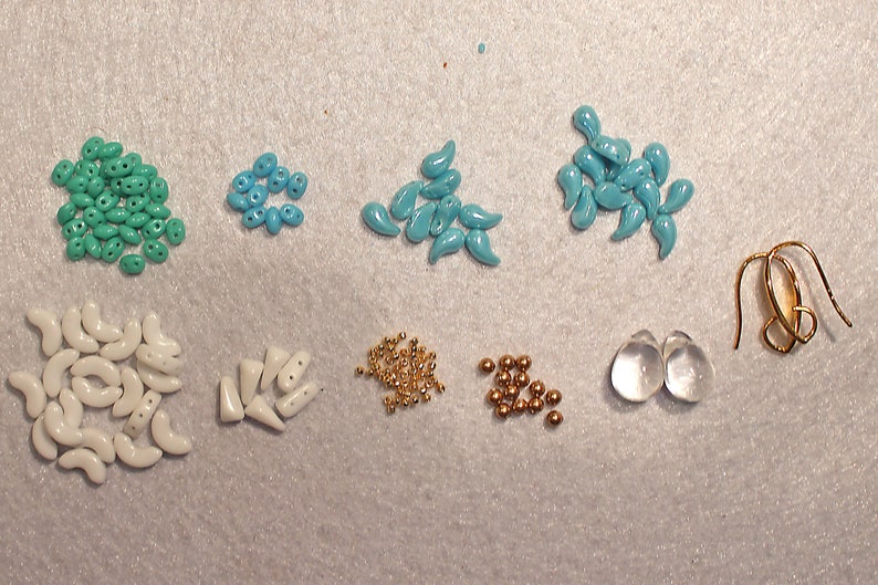 May include: Assortment of turquoise, white, and gold beads, along with two clear glass beads and gold earring hooks. The beads are various shapes, including teardrop, crescent, and round.