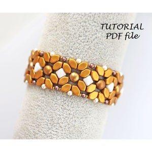 May include: A gold and white beaded bracelet with a geometric pattern. The bracelet is made with small, round beads and larger, faceted beads. The beads are arranged in a repeating pattern of gold, white, and gold. The bracelet is on a white background.