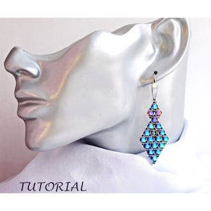 Puede incluir: Un par de pendientes de diamante azul y morado iridiscente con ganchos plateados. Los pendientes están hechos de pequeñas cuentas y cuelgan de la oreja de un maniquí.
