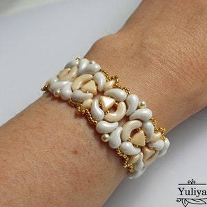 Op de afbeelding: Een witte en beige kralen armband met een geometrisch patroon. De armband is gemaakt met kleine, ronde kralen en grotere, traanvormige kralen.
