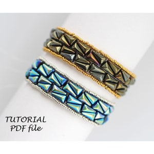 以下が含まれることがあります： 幾何学模様のビーズブレスレットが2つ。 上のブレスレットはダークグレーとゴールドのビーズで作られています。 下のブレスレットはブルーとシルバーのビーズで作られています。 ブレスレットの下に「TUTORIAL PDF file」というテキストが表示されています。