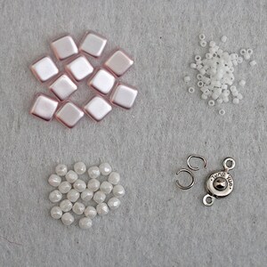 May include: A set of jewelry making supplies including pink square beads, white round beads, and a silver clasp with the text "Tang Yue".