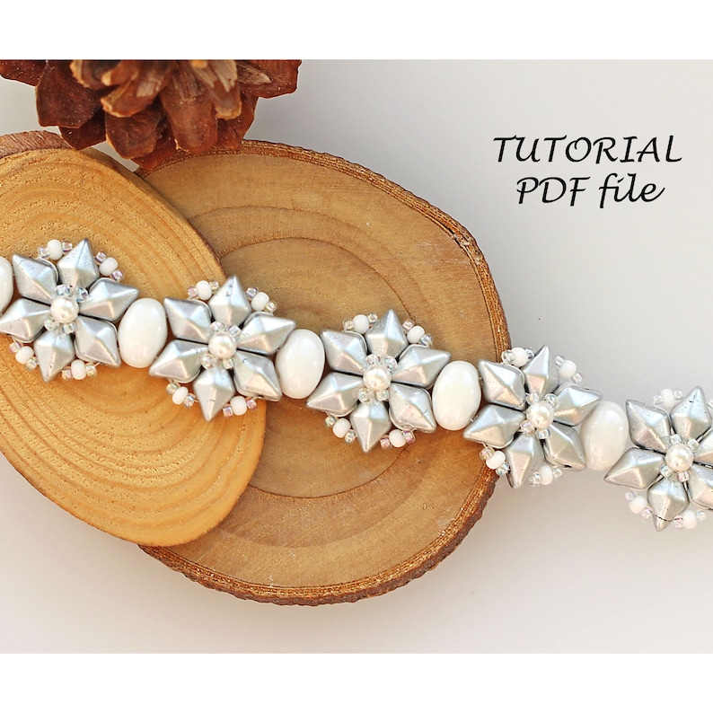 Puede incluir: Un brazalete de cuentas plateadas y blancas con un dise&ntilde;o de flores. El brazalete est&aacute; sobre una superficie de madera. El texto "TUTORIAL PDF file" est&aacute; en la esquina superior derecha de la imagen.