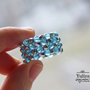 May include: A blue and silver beaded ring. The ring is made of small, faceted beads that are woven together in a spiral pattern.