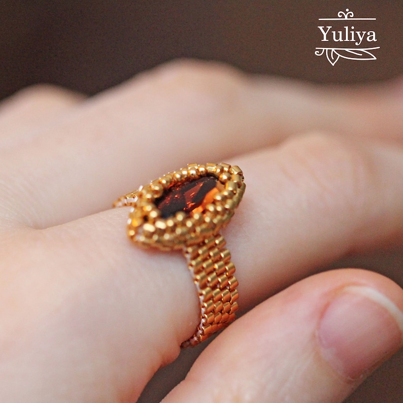 K&ouml;nnte beinhalten: Ein goldfarbener Perlenring mit einem gro&szlig;en, ovalen, dunkelroten Edelstein.