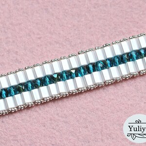 May include: A close-up of a white and teal beaded bracelet. The bracelet is made with small, square white beads and round teal beads. The beads are strung on a silver wire.