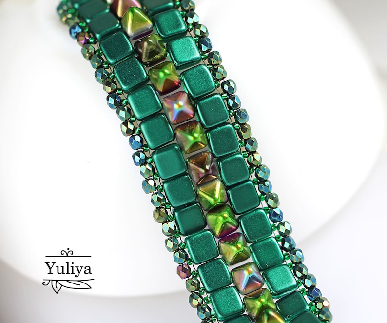May include: A green and iridescent beaded bracelet with a geometric pattern. The bracelet is made with square and triangular beads.