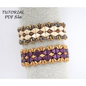 Könnte beinhalten: Zwei Perlenarmbänder mit geometrischen Mustern. Das obere Armband ist aus weißen, braunen und goldenen Perlen gefertigt. Das untere Armband ist aus violetten, goldenen und braunen Perlen gefertigt.