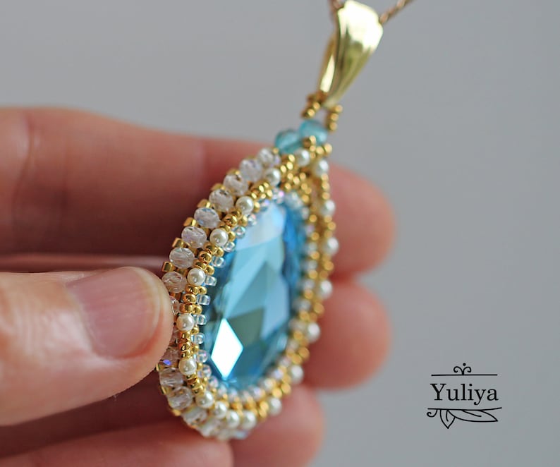 Peut inclure: Un collier avec un pendentif en forme de larme orn&eacute; d'un grand cristal bleu entour&eacute; de perles dor&eacute;es et blanches.