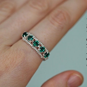 May include: A silver ring with a row of emerald green gemstones. The ring is on a finger.