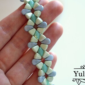 Peut inclure: Gros plan sur un bracelet de perles avec un motif r&eacute;p&eacute;titif de perles en forme de goutte d'eau, de couleur bleu clair, vert menthe et blanc cass&eacute;. Le bracelet est tenu dans une main, mettant en valeur le design et la palette de couleurs. C'est un bijou.