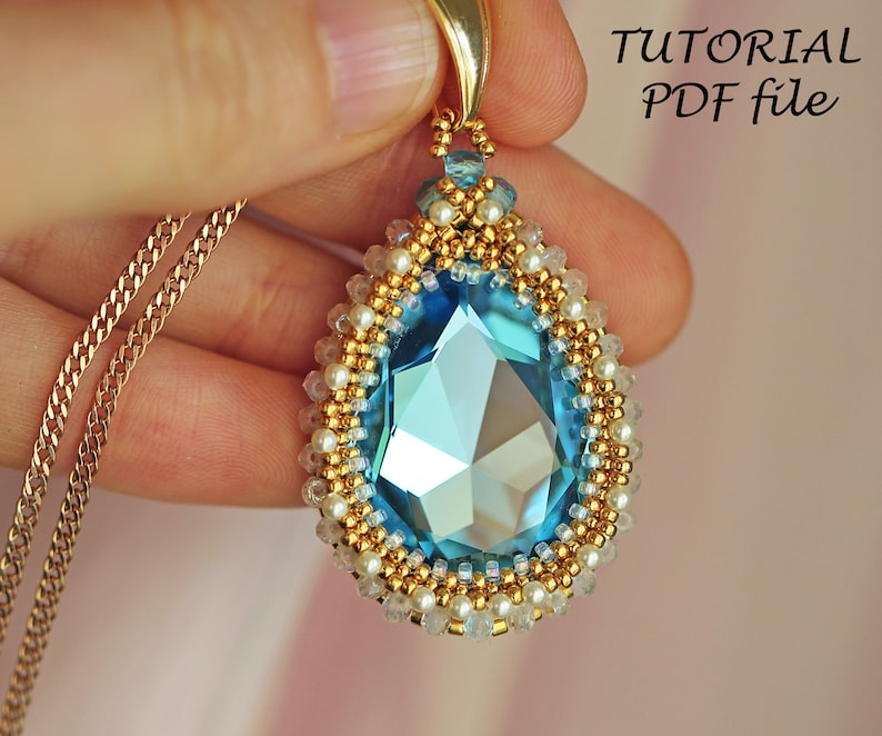 Peut inclure: Un collier avec un pendentif en forme de larme compos&eacute; d'un grand cristal bleu entour&eacute; de perles dor&eacute;es et blanches. Le collier est sur une cha&icirc;ne dor&eacute;e. L'image comprend le texte "TUTORIAL PDF file".