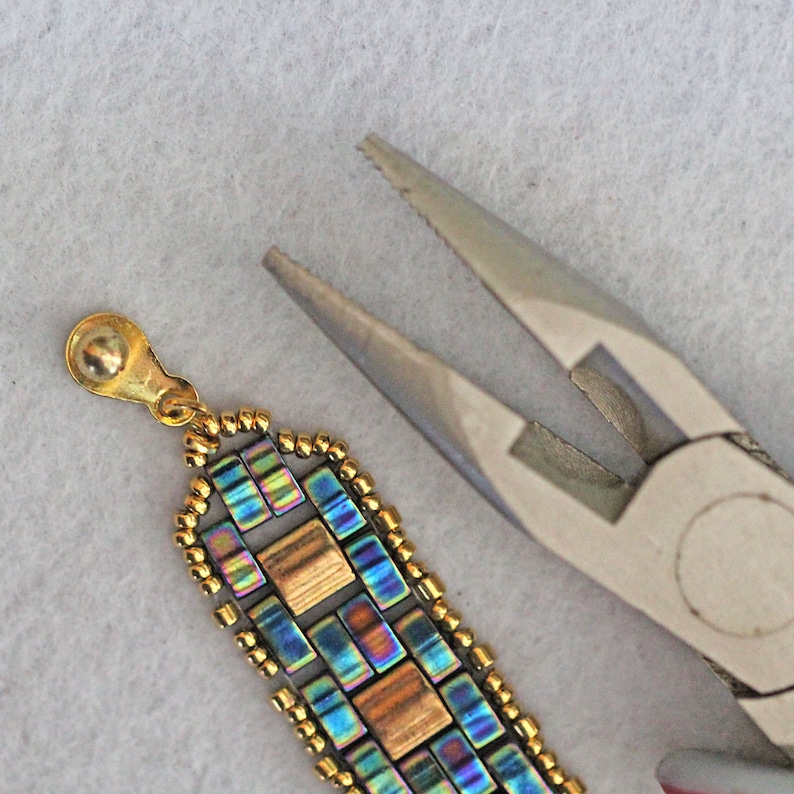 May include: Close-up of a beaded bracelet with a gold clasp being crimped with pliers. The bracelet is made with iridescent blue and gold square beads.