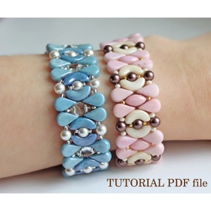 Pode incluir: Duas pulseiras de contas, uma em tons de azul e a outra em rosa e branco, com um acento de contas marrons. As pulseiras estão no pulso de uma pessoa.  TUTORIAL PDF file.
