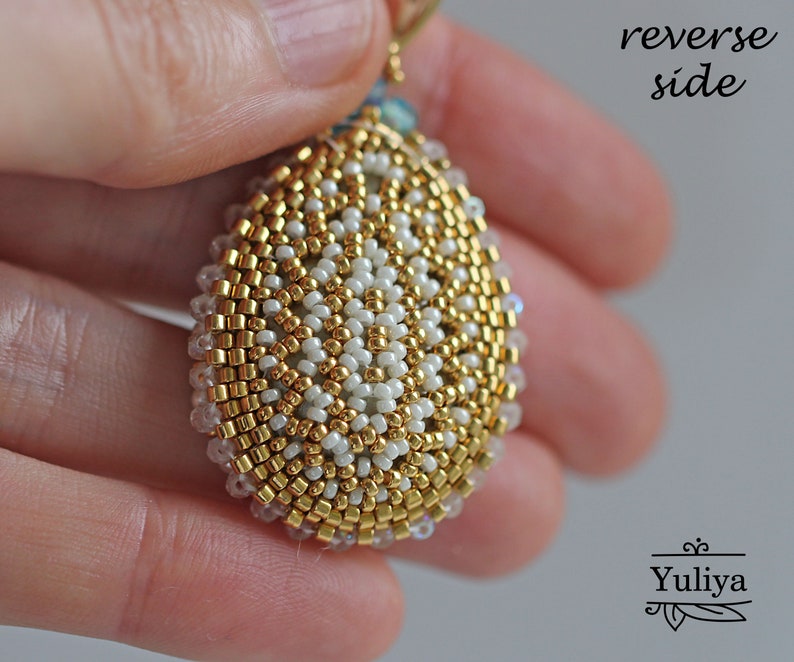 Peut inclure: Gros plan sur l'arri&egrave;re d'un pendentif en forme de larme en perles dor&eacute;es et blanches. Les perles sont dispos&eacute;es en cercle, cr&eacute;ant un motif textur&eacute; et complexe.