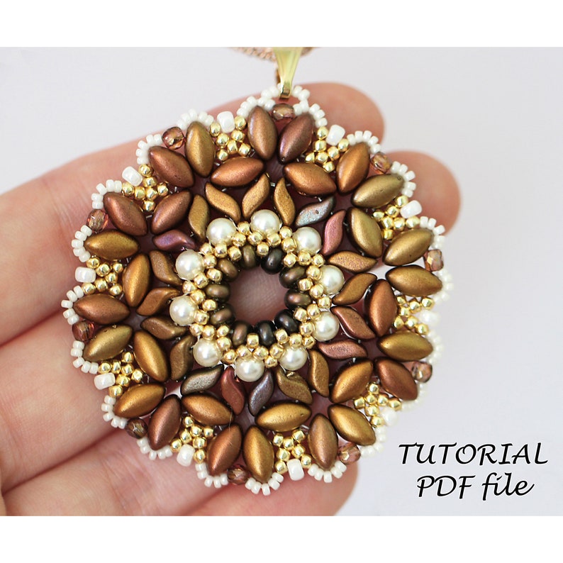May include: A beaded pendant with a gold, brown, and white color scheme. The pendant is in the shape of a flower with a circular center. The pendant is being held in a hand. The text "TUTORIAL PDF file" is visible in the bottom right corner of the image.