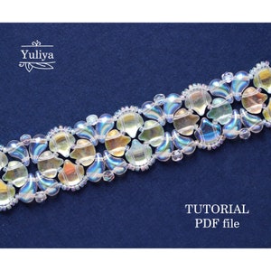 Op de afbeelding: Een kralenarmband met iriserende, traanvormige kralen in tinten blauw, groen en geel. De armband is gemaakt met een herhalend patroon van kralen en wordt getoond op een donkerblauwe achtergrond. De tekst "TUTORIAL PDF file" staat onderaan de afbeelding.