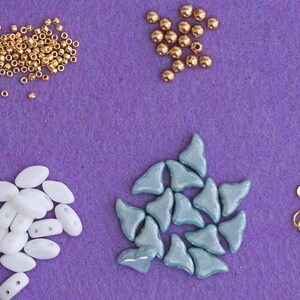 May include: Assortment of beads in various shapes and colours, including gold, white, and blue, along with a gold metal clasp. These beads are perfect for jewellery making.
