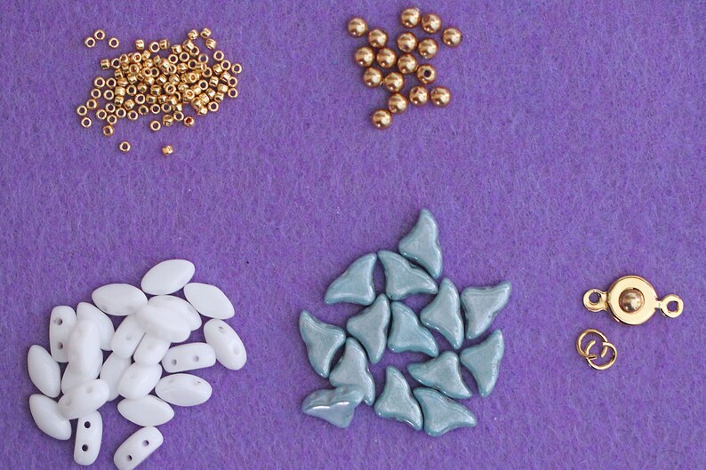 May include: Assortment of beads in various shapes and colours, including gold, white, and blue, along with a gold metal clasp. These beads are perfect for jewellery making.