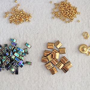 May include: Assortment of gold and iridescent beads, including round, square, and rectangular shapes. Also included are two gold metal clasps.