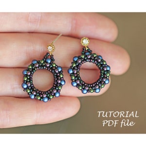 Puede incluir: Un par de pendientes de cuentas con un diseño circular. Los pendientes están hechos con cuentas iridiscentes azules, verdes y negras. Cada pendiente tiene un pequeño cristal transparente en la parte superior.