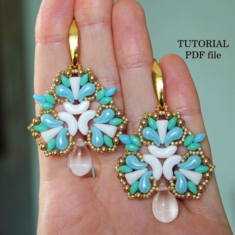 May include: A pair of gold earrings with a teardrop-shaped crystal pendant. The earrings are made with blue, white, and green beads in a geometric pattern. The earrings are shown on a hand, with the text "TUTORIAL PDF file" in the upper right corner.