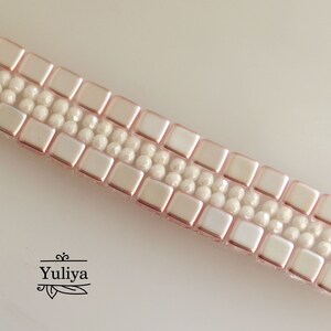 May include: A close-up of a pink and white beaded bracelet. The bracelet is made with square and round beads.