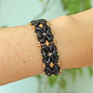 Peut inclure: Un bracelet en perles noires et dor&eacute;es avec un motif g&eacute;om&eacute;trique. Le bracelet est compos&eacute; de petites perles rondes et de perles plus grandes en forme de goutte.