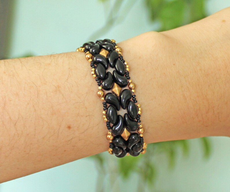 Peut inclure: Un bracelet en perles noires et dor&eacute;es avec un motif g&eacute;om&eacute;trique. Le bracelet est compos&eacute; de petites perles rondes et de perles plus grandes en forme de goutte.