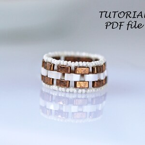 Peut inclure: Une bague en perles blanches et cuivre avec un motif g&eacute;om&eacute;trique. La bague est faite de petites perles blanches et de carr&eacute;s en cuivre. Tutoriel PDF.